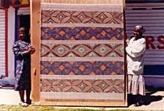 two women standing in front of a large piece of art that is made out of wood