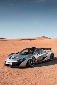 a silver sports car parked in the middle of a desert area with sand dunes behind it