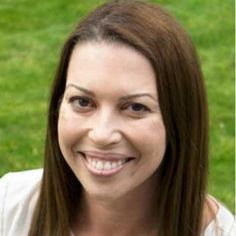 a woman with long brown hair smiling at the camera and wearing a white shirt in front of green grass