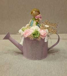 a small figurine sitting on top of a watering can with flowers in it