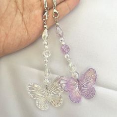 a hand holding a purple butterfly necklace with clear beads and swarong crystals on it