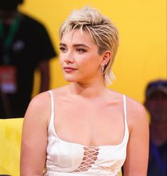 a woman with short blonde hair sitting on a yellow chair in front of a crowd