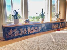 a living room filled with lots of windows next to a firewood rack and potted plants