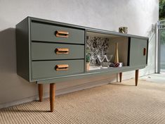 a sideboard with three drawers and gold handles on the bottom, in front of a wall