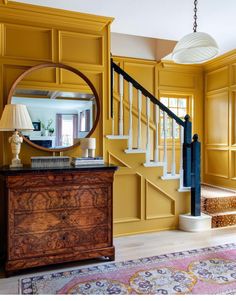 a living room with yellow walls and wooden furniture on the floor, along with a round mirror