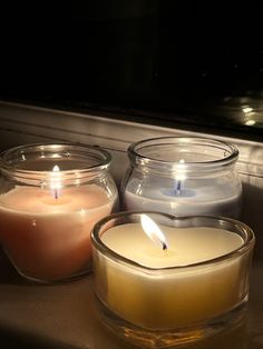 three candles sitting in front of a window sill with one lit up and the other closed