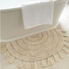 a bathroom rug with tassels on the floor next to a white bath tub