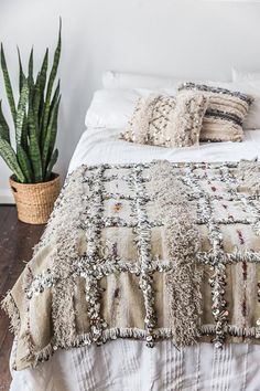 a bed with pillows and blankets on top of it next to a potted plant