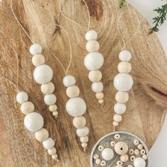 some white beads are hanging on a wooden board next to a metal bowl and sprigs