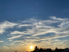 the sun is setting behind some clouds in the sky over a field with houses and trees