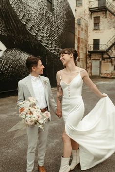 a man and woman in wedding attire holding hands while standing next to each other on the street