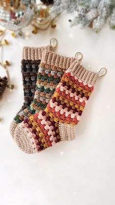 three knitted christmas stockings hanging from hooks on a white table next to pine cones