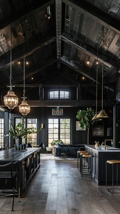 an open kitchen and dining room with wooden floors, black walls and ceiling lights hanging from the rafters