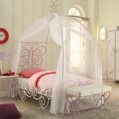 a white canopy bed sitting in a bedroom next to a pink chair and table with a clock on it