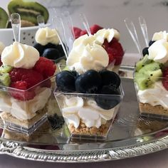 desserts are arranged in small clear containers on a silver platter with fruit and whipped cream