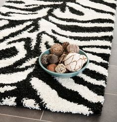 a bowl filled with balls sitting on top of a black and white rug next to a zebra print area rug