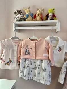 three baby clothes hanging on a rack with teddy bears