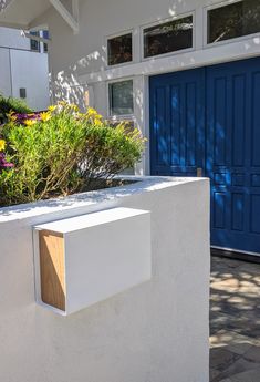 a white wall with a blue door and some plants in front of it on a sunny day