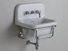 a white sink mounted to the side of a wall with two faucets on it