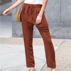 a woman standing on the sidewalk with her hand in her pocket and wearing brown pants