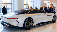 a white sports car is on display in a large room with people looking at it