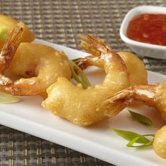 some food is sitting on a white plate with dipping sauce in the bowl behind it