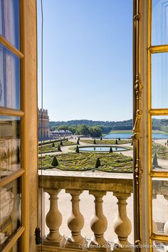 an open door leading to a balcony with a view of a formal garden and lake