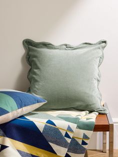 a bed with two pillows on top of it next to a wooden table and white wall