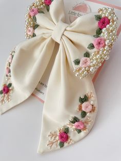 a white bow with pink flowers and pearls on the side is sitting next to a card