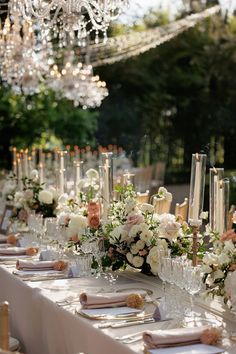 a long table is set with white and pink flowers, candles, and napkins