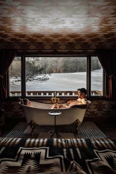 a woman sitting in a bathtub on top of a rug next to a window