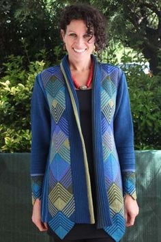 a woman standing in front of a green fence wearing a blue cardigan and black pants