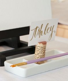 a pen and pencil holder with a name tag on it sitting on a white table cloth