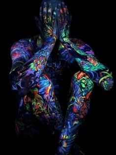 a person covered in colorful paint holding their hands up to their face with both hands