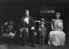 an old black and white photo of three people sitting in chairs with two children standing next to them