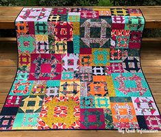 a colorful quilt sitting on top of a wooden table next to a bench and fence