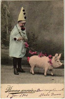 a little boy in a white coat and hat is holding a pig on a leash