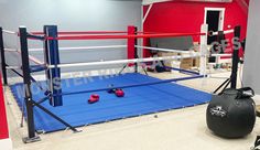 an empty boxing ring with red gloves on the floor and blue mats in front of it