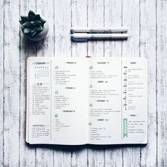 an open planner sitting on top of a wooden table next to a pen and plant