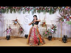 a woman standing on top of a stage in front of a floral wall with lights