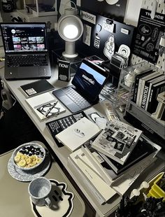 a laptop computer sitting on top of a desk covered in papers and other items next to a lamp