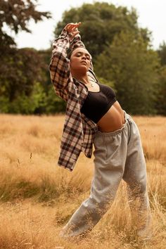 a woman standing in the middle of a field with her hands up to her head