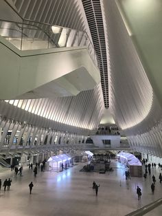 people are walking around in an airport terminal with large ceilings and lights on the ceiling