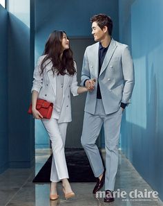 a man and woman walking down a hallway holding hands, both dressed in grey suits