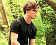 a young man standing in the woods holding a frisbee