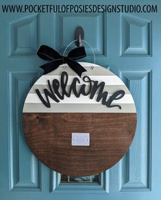 a welcome sign hanging on the front door of a blue door with a black bow