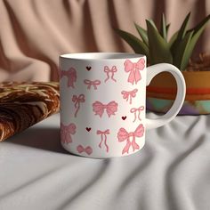 a pink bow coffee mug sitting on top of a table next to a potted plant