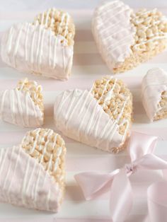 heart shaped cookies with white frosting on a pink and white striped tablecloth next to a bow