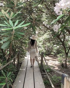 a woman walking across a wooden bridge surrounded by trees