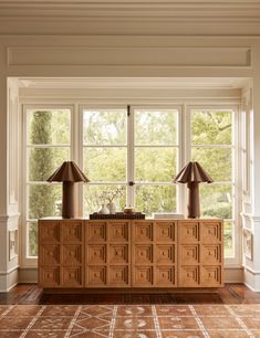 two lamps are on top of a wooden cabinet in front of a large window with windows